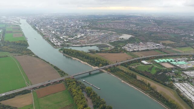 High angle perspective showing the rhine river flowing through the german landscape, with bridges connecting rural fields to the vast industrial port and cityscape of ludwigshafen
