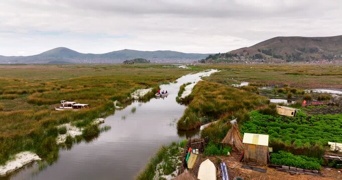 Uros floating islands on Lake Titicaca, Peru. Shows traditional reed homes, boats, and the surrounding wetlands. Aerial backward