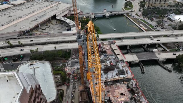 Large construction crane over downtown Tampa, showing bridges, traffic flow, riverfront infrastructure and active port area in urban American city environment. Aerial tilt down top view.