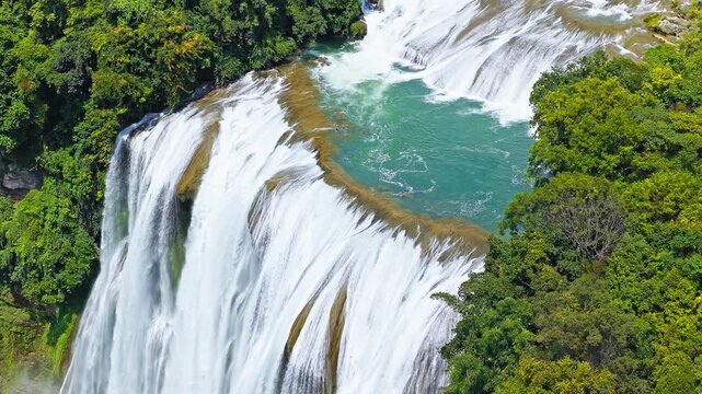 Aerial view of the famous Huangguoshu Waterfall in Guizhou, China, featuring majestic water cascading into a blue river surrounded by lush green forest.