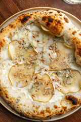 Italian style pizza topped with sliced pear gorgonzola cheese and creamy white sauce served on wooden table