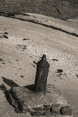 Ancien pieu métallique rouillé planté dans un bloc de pierre au bord d’une plage,...
