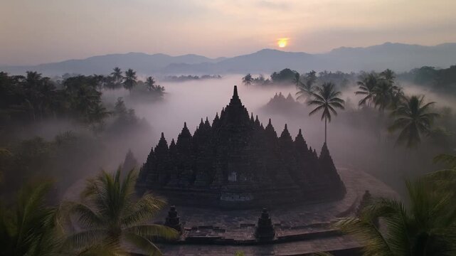 Misty Morning Sunrise Over Ancient Borobudur Temple with Palm Trees and Foggy Atmosphere