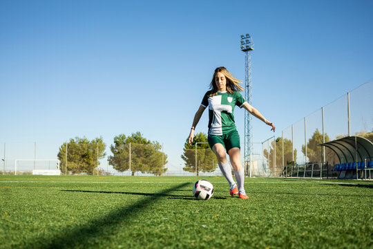 A Caucasian girl between 20 and 30 years old wearing green sportswear is playing soccer on a grass field.The girl is dribbling on the soccer field. Concept of women's soccer.
