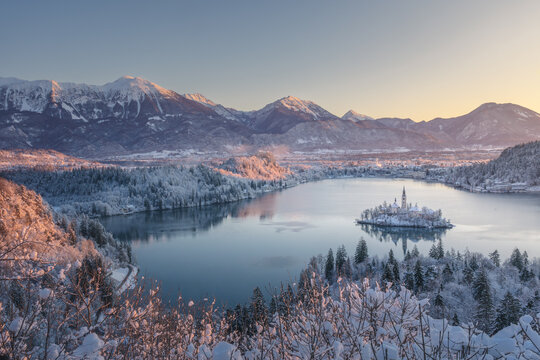 Aerial view of the serene Lake Bled and its iconic island church, embraced by snow-laden forests and majestic mountains, Bled, Radovljica, Slovenia.