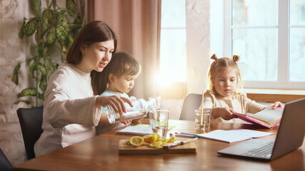 Mother pouring water for children at kitchen table. Concept of family hydration routine, healthy drinking habits, daily water intake, home lifestyle, and caring parent support.