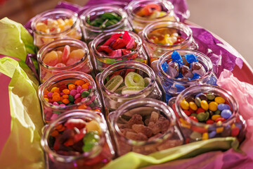 Fototapeta premium A festive assortment of colorful candies arranged in clear glass jars, wrapped in vibrant tissue paper, ideal for a candy buffet or event decor. Copy space included