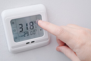 Hand adjusting temperature on a digital wall thermostat for underfloor heating.