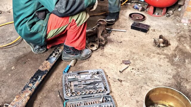 Mechanics repairing vehicle suspension part on dirty workshop floor with tool kit