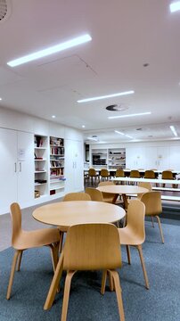 Modern Office Meeting Area With Empty Round Tables And Wooden Chairs White Walls And Shelves Nobody Present For Corporate Or Educational. vertical video
