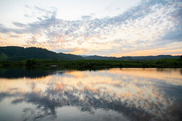 Obraz premium Serene moment of a sunset over the Daintree river surrounded by lush green hills. The sky is filled with soft, colorful clouds, and the water reflects the warm light of the sun. Daintree in Queenslan