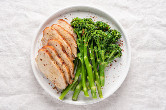 Minimalist healthy meal with green broccolini and roasted turkey breast served on a white plate on a linen tablecloth