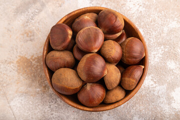wooden bowl with raw edible Сhestnuts on brown concrete, top view, flat lay, close up, minimalism