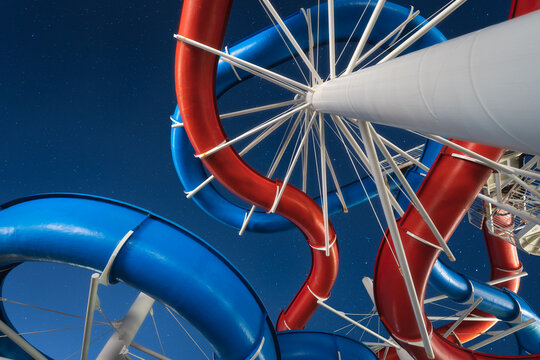 View of vibrant red and blue intertwined water slides spiraling against a deep blue sky, supported by a white structure, Izola, Slovenia.