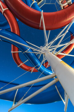 View of a dizzying swirl of red and blue water slides twisting against a vibrant blue sky, captured from a low angle, Izola, Slovenia.