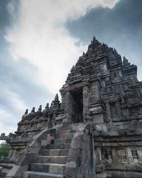 View of a majestic gray stone temple ascends to meet the turbulent sky, ancient steps leading into shadow, a testament to time and devotion, Magelang Regency, Indonesia.