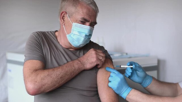 Elderly Man in Face Mask getting Covid Vaccine. Doctor giving Injection to senior Man at Hospital.