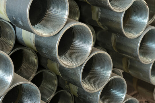 Close-up of stacked steel pipes with internal threading visible on the ends stored inside an industrial metal warehouse