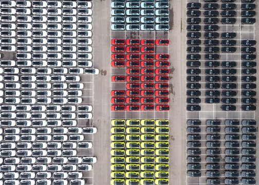 Aerial view of a sea of colorful new cars meticulously arranged in rows, creating a vibrant tapestry of hues against the stark concrete, Palmachim, Center District, Israel.