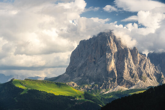 View of dramatic Dolomites peak piercing through swirling clouds, bathed in soft light with verdant slopes below, Urtijei, Trentino-South Tyrol, Italy.