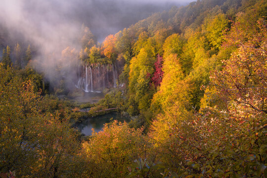 View of a vibrant autumn forest embracing misty waterfalls and tranquil lakes in Plitvicka Jezera, Lika-Senj County, Croatia.