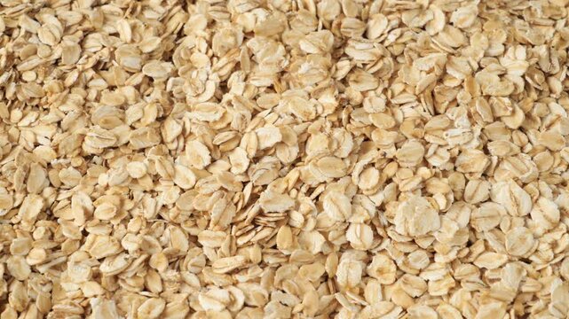 Raw oatmeal flakes pouring down creating a healthy whole grain food background texture.