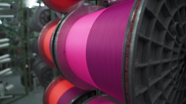 large spools of pink and orange thread spinning in a textile factory
