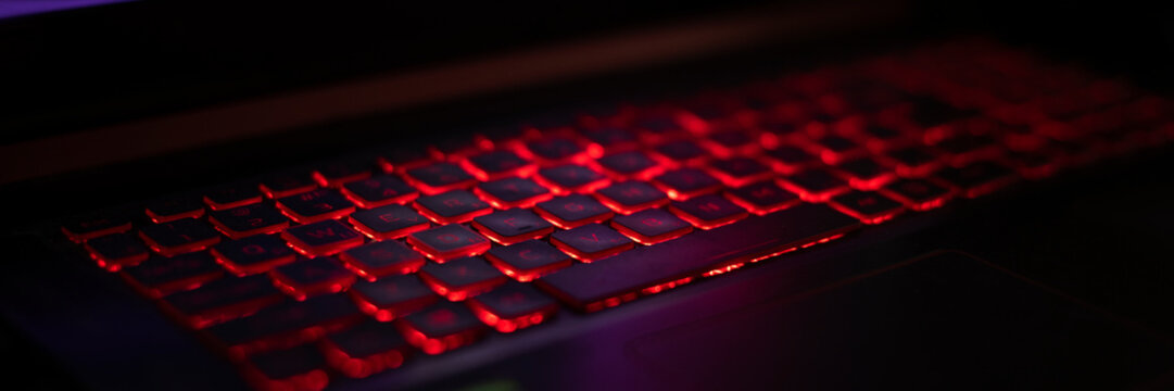 A close-up view of a laptop keyboard illuminated with red backlighting. The keys are sleek and modern, set against a dark background. banner