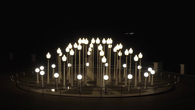 white street lamps with glowing spherical globes on dark paved plaza within metal fence at night.