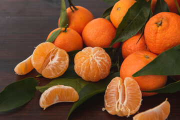 Fresh tangerines with leaves spilling out of a brown paper bag on dark wooden table