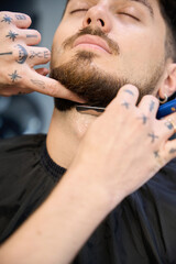 Fototapeta premium Stylist shapes beard, using compact razor with care
