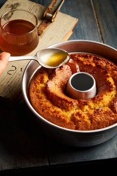 A hand drizzling syrup with a spoon over a round cake on a blue wooden table