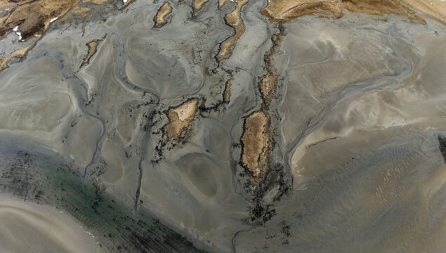 Aerial view of a tapestry of muted earth tones interwoven with the stark contrast of dark, winding rivulets, creating an ethereal, otherworldly landscape, Selfoss, Iceland.
