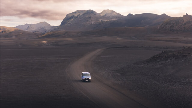 Aerial view of a solitary van navigating a desolate, winding road across a dark, volcanic landscape under a muted sky, Selfoss, Iceland.