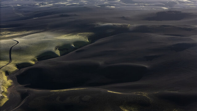 Aerial view of dark volcanic sand plains, with patches of green moss and winding river channels cutting through the landscape, Selfoss, Iceland.