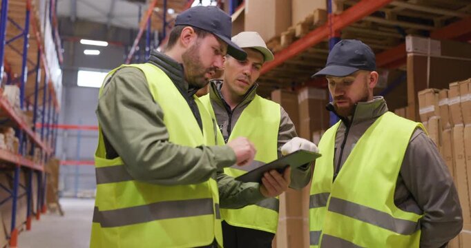 Workers supervisors discuss logistics on warehouse floor. Wearing safety vests, they review planning on a clipboard, align inventory checks and shipping tasks. Teamwork keeps logistics on track.
