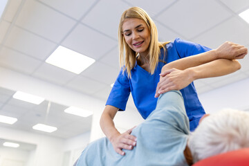 Obraz premium Female physical therapist stretching the arm and shoulder of a senior woman on a treatment table. Professional rehabilitation session for elderly mobility in a bright modern medical clinic.