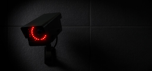 Black CCTV Security Camera with Red LED Lights on Dark Wall