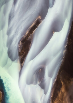 Aerial view of glacial rivers paint abstract patterns across the landscape, creating a marbled effect of white and brown, Iceland.