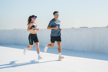 Young adults run on a rooftop in bright sunlight while enjoying their active lifestyle together