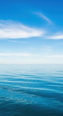 Fototapeta premium Vast blue ocean surface with gentle waves under a clear sky with wispy clouds