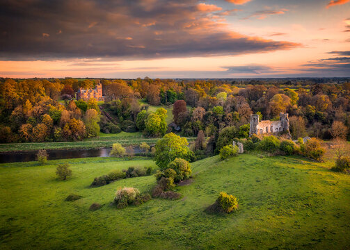 Aerial view of a serene landscape with ancient ruins and lush greenery bathed in the warm glow of the setting sun, Adare, Ireland.
