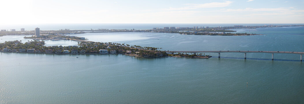 Aerial view of turquoise waters meet sandy shores and Ringling Bridge stretches across the bay, connecting islands dotted with buildings, Sarasota, Florida, United States.