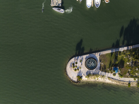 Aerial view of a circular pier jutting into the dark waters, boats dotting the scene, a dance of light and shadow on the water's surface, Sarasota, United States.