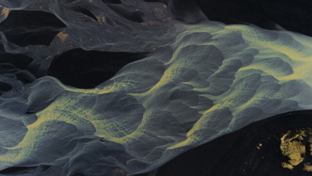 Aerial view of glacial river patterns weave through black sands, creating ethereal textures in a stark, contrasting landscape, Selfoss, Iceland.
