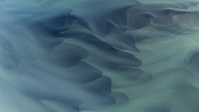 Aerial view of glacial rivers intertwine in mesmerizing patterns, their icy blues and greens creating an ethereal dance across the rugged landscape, Selfoss, Iceland.