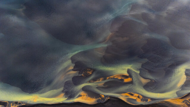 Aerial view of glacial rivers intertwining like veins across the land, with their contrasting colors creating an otherworldly landscape, Selfoss, Iceland.