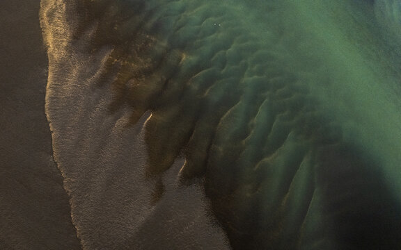 Aerial view of the braided river's turquoise waters meet the dark, volcanic sands in a mesmerizing dance of color and texture, Selfoss, Iceland.