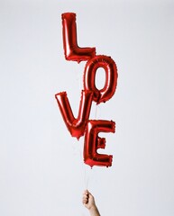 hand holding vertical stack of red foil balloons spelling love for valentine's day wedding and romantic celebration isolated on white background