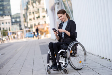 Obraz premium Smiling businesswoman in a wheelchair using smart phone working outdoors